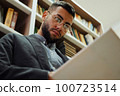 Man in eyeglasses reading book in library 100723514
