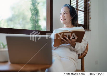 Portrait of an elderly Asian woman in a modern pose holding a memory notebook and operating a computer 100723558