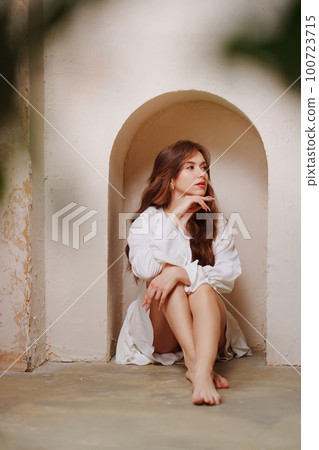 a woman in a white dress barefoot sitting on the floor in an arch on the wall a woman in a white dress barefoot sitting on the floor in an arch on the wall 100723715