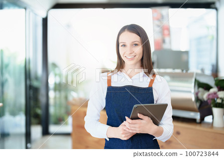 Starting and opening a small business, a young Asian woman showing a smiling face in an apron standing in front of a coffee shop bar counter. Business Owner, Restaurant, Barista, Cafe, Online SME. 100723844
