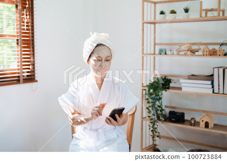 Portrait of elderly woman doing face spa treatment and using mobile phone 100723884
