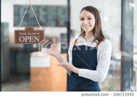 Starting and opening a small business, a young Asian woman showing a smiling face in an apron standing in front of a coffee shop bar counter. Business Owner, Restaurant, Barista, Cafe, Online SME. 100723930