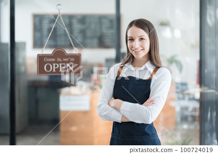 Starting and opening a small business, a young Asian woman showing a smiling face in an apron standing in front of a coffee shop bar counter. Business Owner, Restaurant, Barista, Cafe, Online SME. Starting and opening a small business, a young Asian woman showing a smiling face in an apron standing in front of a coffee shop bar counter. Business Owner, Restaurant, Barista, Cafe, Online SME. 100724019