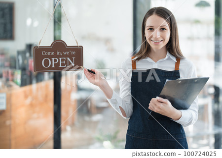 Starting and opening a small business, a young Asian woman showing a smiling face in an apron standing in front of a coffee shop bar counter. Business Owner, Restaurant, Barista, Cafe, Online SME. Starting and opening a small business, a young Asian woman showing a smiling face in an apron standing in front of a coffee shop bar counter. Business Owner, Restaurant, Barista, Cafe, Online SME. 100724025