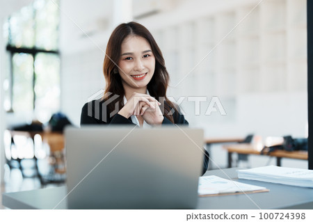 Portrait of a woman business owner showing a happy smiling face as he has successfully invested her business using computers and financial budget documents at work. 100724398