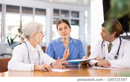 three positive doctors are sitting at table animatedly and actively discussing current work 100725397