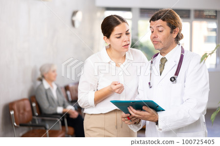 Doctor consulting young female patient filling medical form 100725405