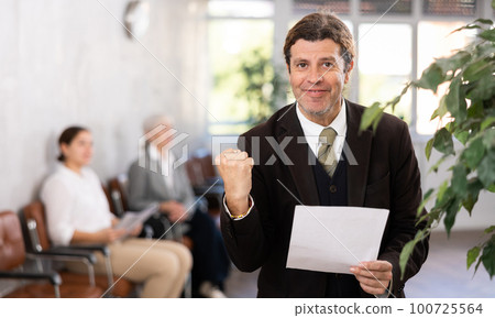 Happy man with papers making woohoo gesture in office Happy man with papers making woohoo gesture in office 100725564