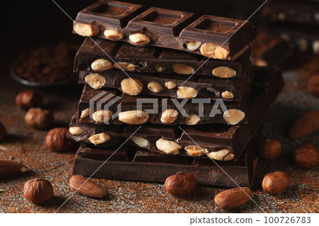 Dark and milk chocolate with nuts on a dark background sprinkled with cocoa powder. Dark and milk chocolate with nuts on a dark background sprinkled with cocoa powder. 100726783