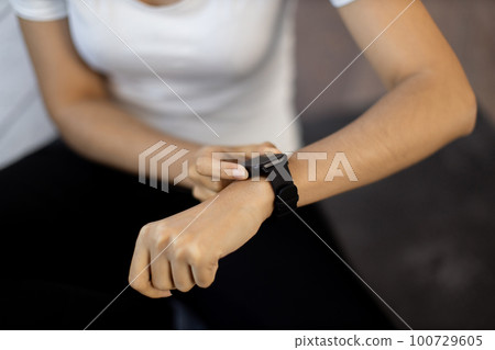 Sporty lady resetting fitness tracker while sitting on floor 100729605