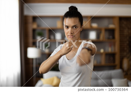 Strong woman in sport outfit practising in boxing at flat Strong woman in sport outfit practising in boxing at flat 100730364