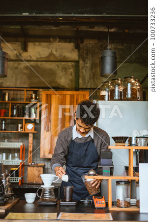 the male barista seriousely pouring the coffee into the glass the male barista seriousely pouring the coffee into the glass 100733236