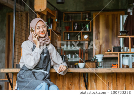 female barista with hijab calling someone using the phone 100733258