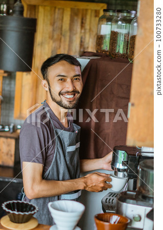 male barista in apron standing with smile while operating the coffee machine 100733280