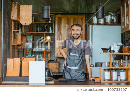 male barista in apron standing with smile inside the bar desk 100733307