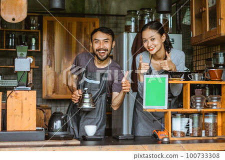 a couple of barista standing with thumbs up inside the bar desk 100733308