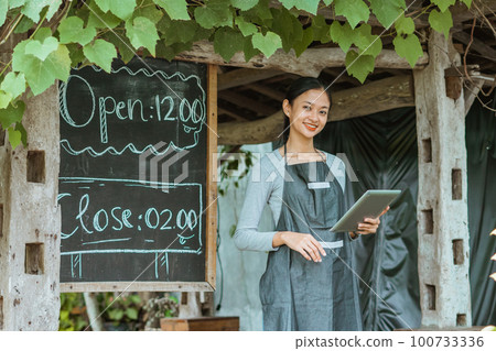 female barista using the digital tablet while standing outside the coffee shop female barista using the digital tablet while standing outside the coffee shop 100733336