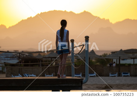 Young woman in casual outfit relaxing on seaside on warm evening. Summer vacations and travelling concept. Young woman in casual outfit relaxing on seaside on warm evening. Summer vacations and travelling concept. 100735223