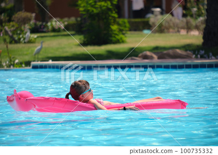 Young child girl relaxing on summer sun swimming on inflatable air mattress in swimming pool during tropical vacations. Summertime activities concept 100735332