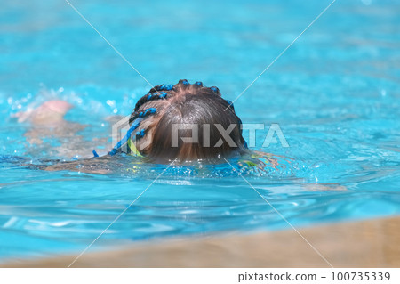 Young child girl in goggles exercises swimming in blue pool water. Summer recreation activity concept 100735339