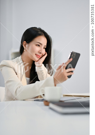 Beautiful Asian businesswoman using her phone, scrolling on social media or using mobile app 100735381