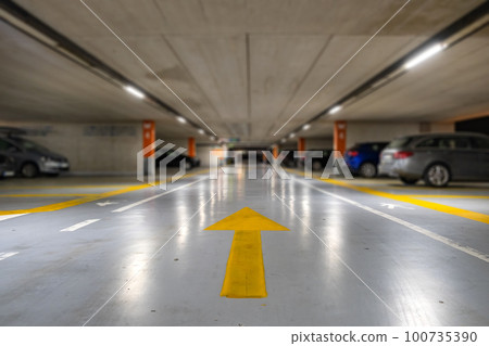 Yellow markings with blurred modern cars parked inside closed underground parking lot. 100735390
