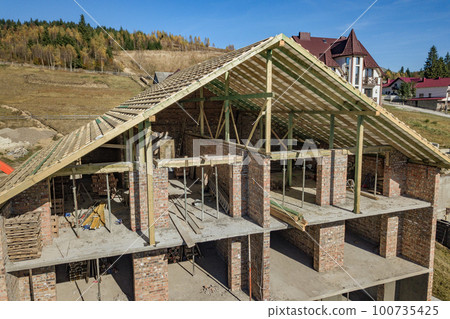 Wooden frame of new roof on a brick big house under construction. Wooden frame of new roof on a brick big house under construction. 100735425