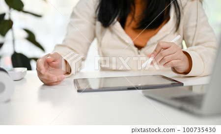 Cropped image of an Asian woman using her digital tablet at her desk. 100735430