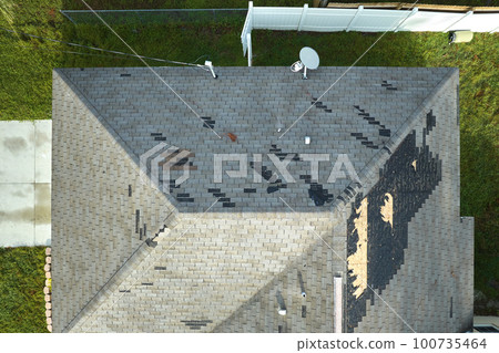 Wind damaged house roof with missing asphalt shingles after hurricane Ian in Florida. Repair of home rooftop concept 100735464