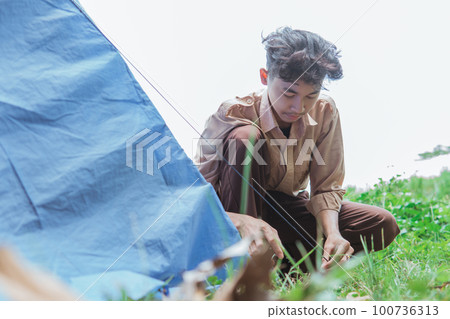a teenage boy wearing scout clothes set up tent pegs a teenage boy wearing scout clothes set up tent pegs 100736313