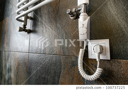 White contemporary electric towel dryer mounted on black tiled wall in modern bathroom. White contemporary electric towel dryer mounted on black tiled wall in modern bathroom. 100737225