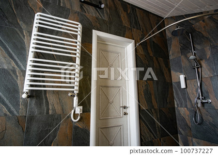 White contemporary electric towel dryer mounted on black tiled wall in modern bathroom. White contemporary electric towel dryer mounted on black tiled wall in modern bathroom. 100737227