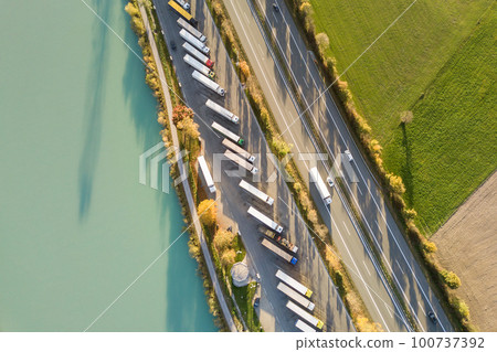 Top down aerial view of highway interstate road with fast moving traffic and parking lot with parked lorry trucks. 100737392