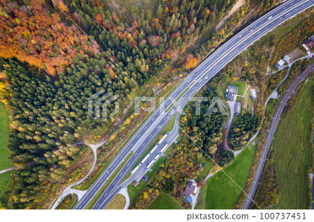 Top dawn aerial view of freeway speed road between yellow autumn forest trees in rural area. 100737451