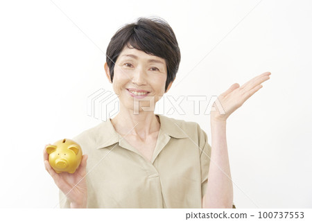 A middle-aged woman holding a piggy bank and pointing to the right with her palm White background 100737553