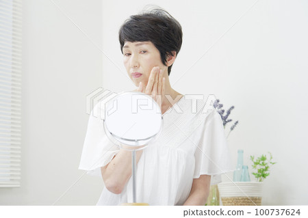 A middle-aged woman who is worried about looking at her face in the mirror A middle-aged woman who is worried about looking at her face in the mirror 100737624