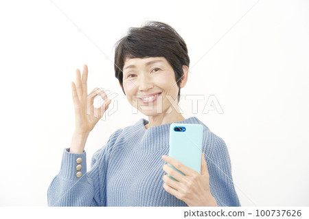 中年婦女拿著智能手機並簽署 OK 白色背景 100737626