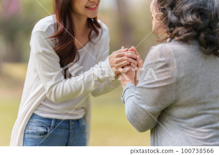 Close up of Adult daughter holding her elderly mother hand with love and walk together Close up of Adult daughter holding her elderly mother hand with love and walk together 100738566