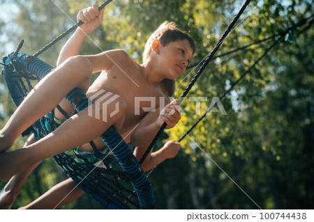 sad and depressed caucasian boy sitting on net swing. Boys small fight sad and depressed caucasian boy sitting on net swing. Boys small fight 100744438
