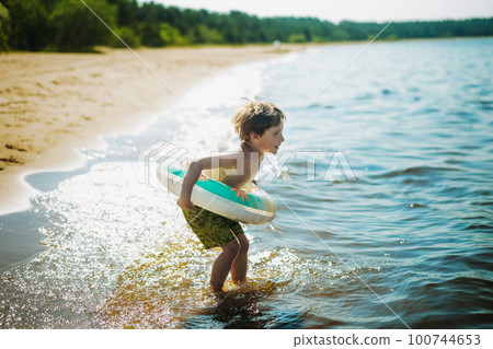 cute caucasian boy running into water with splashes and laughter. Vacation on sea side. Happy childhood. Image with selective focus 100744653