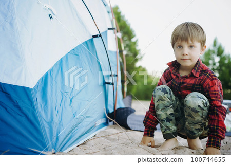 cute little caucasian boy sitting on sand barefoot by touristic tent. Family camping concept 100744655