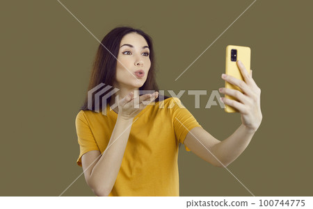 Pretty young woman holding her modern cellphone, blowing air kiss and taking selfie Pretty young woman holding her modern cellphone, blowing air kiss and taking selfie 100744775