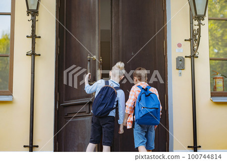 children entering school opening big wooden door. Boys with backpacks by school on sunny day children entering school opening big wooden door. Boys with backpacks by school on sunny day 100744814