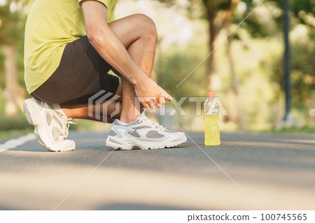 Young athlete man tying running shoes with Energy Drink water, male runner ready for jogging outside, asian Fitness walking and exercise in the park morning. wellness, wellbeing and sport concepts Young athlete man tying running shoes with Energy Drink water, male runner ready for jogging outside, asian Fitness walking and exercise in the park morning. wellness, wellbeing and sport concepts 100745565