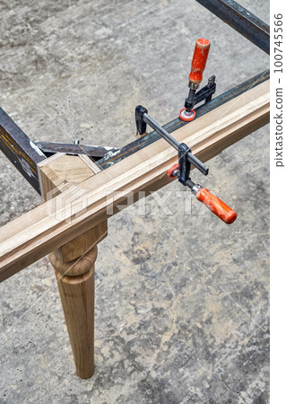 Wooden carved leg of solid oak with metal table frame during manufacturing process of dining table in workshop close up view Wooden carved leg of solid oak with metal table frame during manufacturing process of dining table in workshop close up view 100745566
