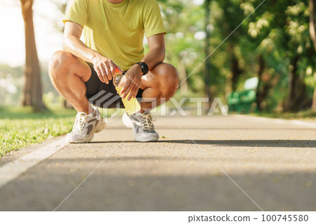 man jogging and walking on the road at morning with Energy Drink water, adult male in sport shoes running in the park outside. Exercise, wellness, healthy lifestyle and wellbeing concepts 100745580