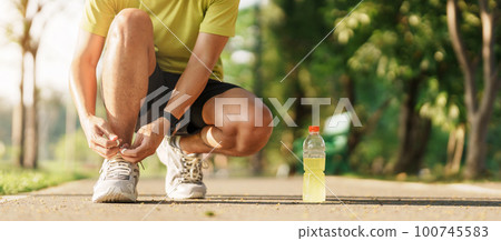 Young athlete man tying running shoes with Energy Drink water, male runner ready for jogging outside, asian Fitness walking and exercise in the park morning. wellness, wellbeing and sport concepts Young athlete man tying running shoes with Energy Drink water, male runner ready for jogging outside, asian Fitness walking and exercise in the park morning. wellness, wellbeing and sport concepts 100745583