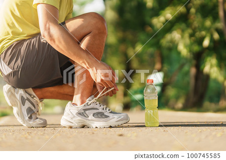 Young athlete man tying running shoes with Energy Drink water, male runner ready for jogging outside, asian Fitness walking and exercise in the park morning. wellness, wellbeing and sport concepts Young athlete man tying running shoes with Energy Drink water, male runner ready for jogging outside, asian Fitness walking and exercise in the park morning. wellness, wellbeing and sport concepts 100745585