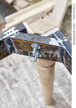 Wooden carved leg of solid oak with metal table frame during manufacturing process of dining table in workshop close up view Wooden carved leg of solid oak with metal table frame during manufacturing process of dining table in workshop close up view 100745615