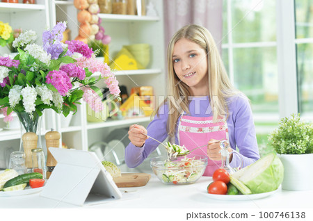 girl preparing fresh salad on kitchen table with tablet at home girl preparing fresh salad on kitchen table with tablet at home 100746138
